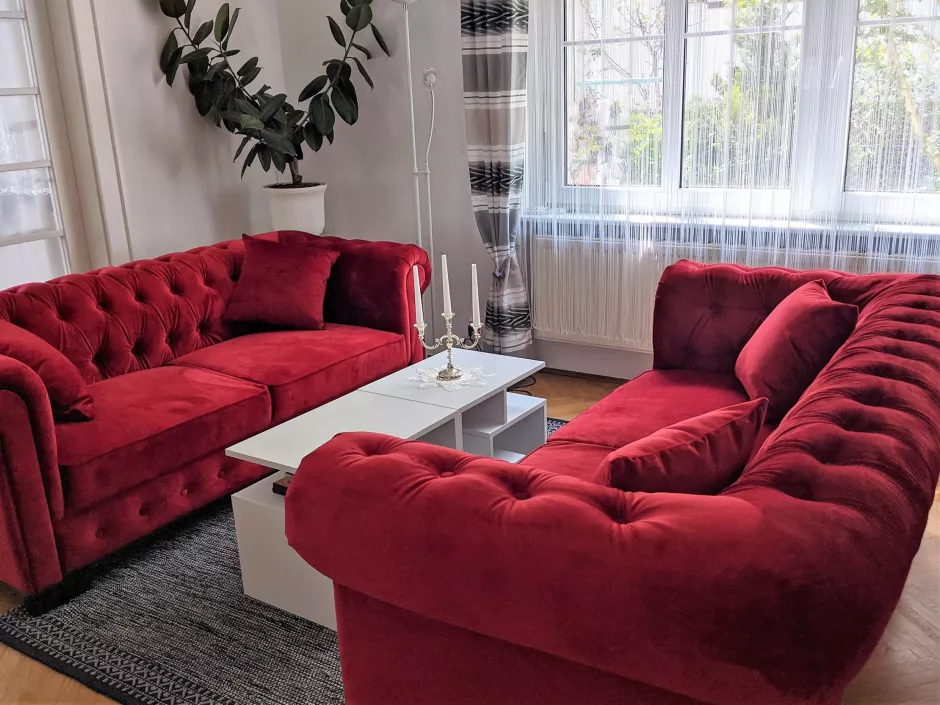Zimmer mit zwei roten Biedermeyer-Sofas und kleinem weißen Tisch, große Pflanze im Hintergrund
