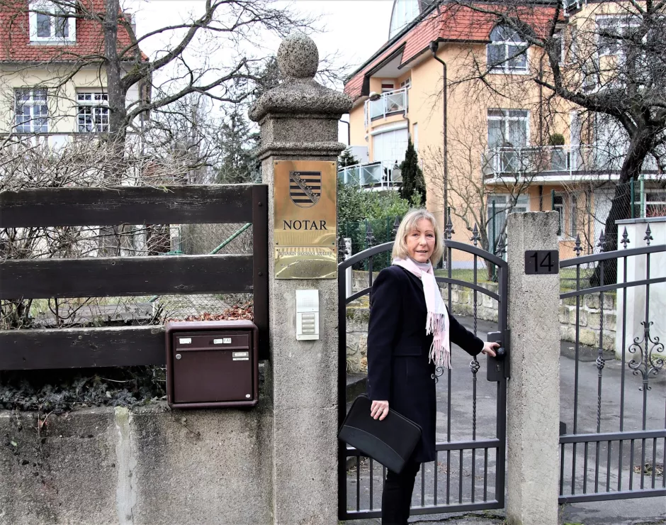 Blonde Frau mit blauem Wintermantel vor dem Tor des Notariats