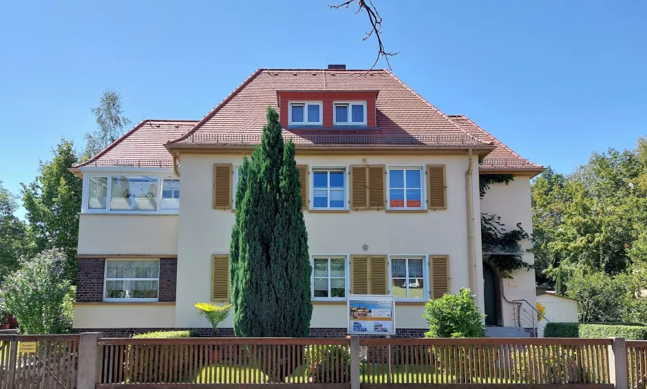 Schönes Mehrfamilienhaus, gelber Anstrich mit Fensterläden, Wintergarten im Obergeschoss und Dachgaube